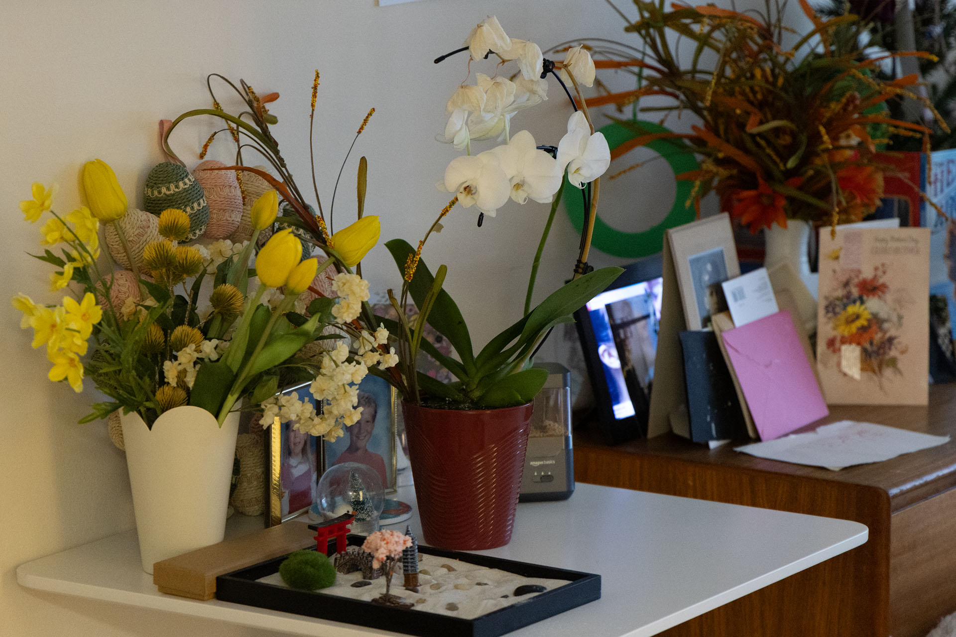 Dresser top decorated with fresh flowers, family photos, greeting cards, and a small zen garden in a resident's room